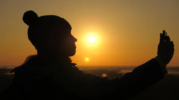 Mujer sana alegre viaja al amanecer y la naturaleza de la fotografía en el teléfono. gratis Jovencita bloguera turística graba un video selfie en la cima de las montañas utilizando un teléfono inteligente con un hermoso paisaje. —  Fotos de Stock