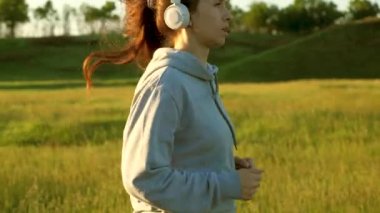 Özgür genç kadın yazın şafakta parkta antrenman yapıyor. Sağlıklı güzel kız spor yapıyor, kırsalda koşuyor. Koşucu kız temiz hava soluyor. Güneşin güzel ışıklarında akşam koşusu.