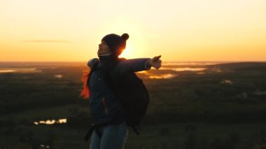 Özgür kız turist doğada yalnız seyahat eder. Sırt çantalı genç bir gezgin gün doğumunun zirvesine gelir, ellerini kaldırır ve döner, zaferin tadını çıkarır, güzel şafak ve manzara..
