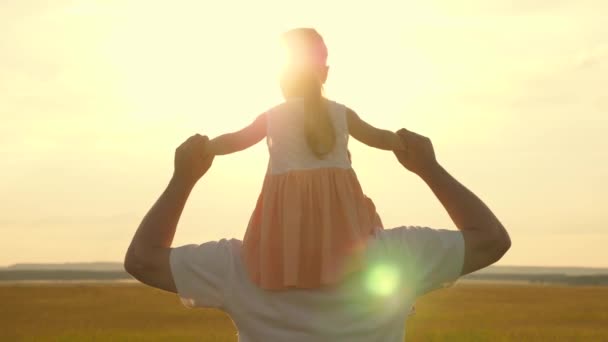 Papá lleva sobre los hombros de su amado hijo, en rayos de sol. Padre camina con su hija sobre sus hombros en rayos de atardecer. niño con padres camina al atardecer. familia feliz descansando en el parque. — Vídeos de Stock