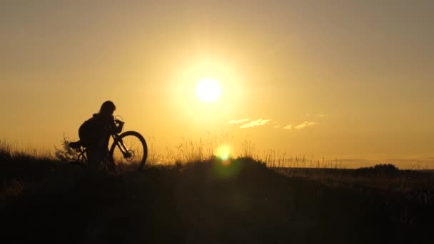 Mujer ciclista supera un obstáculo. chica libre viaja con una bicicleta en la puesta del sol. Turista joven sana va con bicicleta a lo largo de la ladera, disfrutando de la naturaleza, aire fresco. concepto de aventura y viaje . — Vídeo de stock