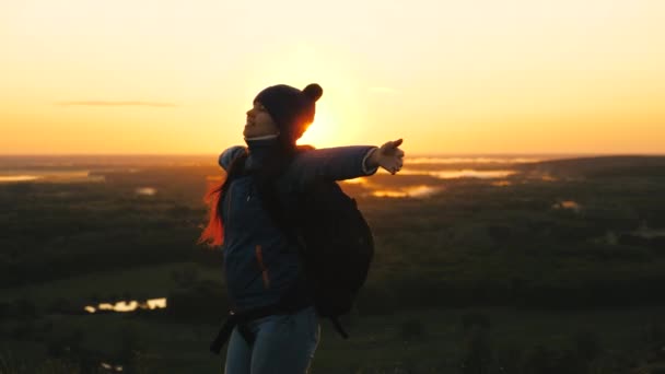 Chica libre turista viaja en la naturaleza solo. joven viajera con una mochila llega al borde de la cima del amanecer, levanta las manos en el aire y gira, disfruta de la victoria, hermoso amanecer y paisaje . — Vídeo de stock