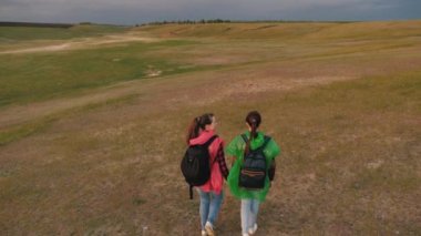 Özgür kadın gezginler vadiye gider. Takım çalışması gezginleri. Macera ve seyahat kavramı. Sağlıklı turist kızları renkli yağmurluklarla sırt çantalarıyla seyahat ederler. Fırtına yaklaşıyor..