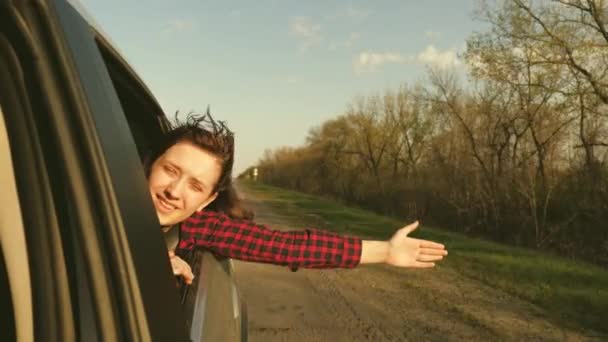 Una ragazza con i capelli lunghi siede sul sedile posteriore di un'auto, tira la mano fuori dal finestrino e cattura lo sguardo del sole al tramonto. Una donna libera viaggia in auto, afferra il vento con la mano dal finestrino dell'auto. — Video Stock