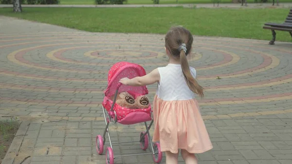 Concept d'enfance saine. petite fille se promène dans le parc avec une poussette et un ours en peluche. Un gamin dans la rue avec son jouet préféré. l'enfant joue dans l'aire de jeux. — Photo