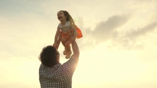 Otec a malé dítě si hrají, smějí se a objímají. Táta vyhazuje šťastnou dceru na modrou oblohu. Šťastná rodina cestuje. Dítě v náručí rodiče. Den volna. Koncept šťastné rodiny — Stock video