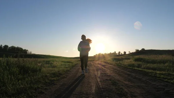 Sport för att bränna kalorier och gå ner i vikt. ung kvinna tränar på sommaren i parken i gryningen i hörlurar med musik. Gratis vacker flicka är engagerad i fitness. Jogger flicka andas frisk luft — Stockfoto