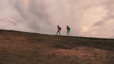 Özgür kadın gezginler tepenin üstünde yürürler. Gezginlerin takım çalışması. Macera ve seyahat kavramı. Sağlıklı kadın turistler sırt çantalarıyla renkli yağmurluklarla seyahat ediyorlar. Fırtına yaklaşıyor.