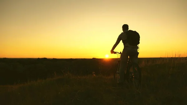 Hiker healthy young man rides a bicycle to edge of the hill, enjoying nature and sun. A free traveler travels with a bicycle at sunset. concept of adventure and travel. lonely cyclist resting in park. — Stock Photo, Image