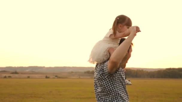 Papà porta sulle spalle del suo amato bambino, in raggi di sole. Padre cammina con la figlia sulle spalle in raggi di tramonto. bambino con genitori cammina al tramonto. famiglia felice che riposa nel parco. — Video Stock