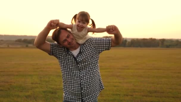 Отец ходит с дочерью на плечах в лучах заката. Папа носит на плечах своего любимого ребенка, в лучах солнца. ребенок с родителями гуляет на закате. счастливая семья отдыхает в парке. — стоковое видео