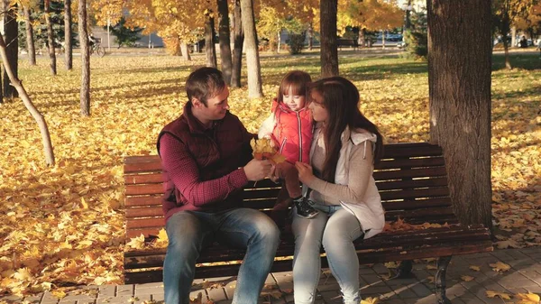 Papa, kleine Tochter und Mama spielen im Herbstpark auf einer Bank. Konzept einer glücklichen Kindheit. Baby, Mutter und Vater spielen mit Herbst-Ahornblättern. Glückliche Familie mit Kind spaziert im Stadtpark. — Stockfoto