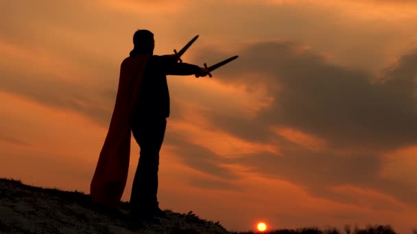 Egy győztes karddal a kezében és piros köpenyben áll egy hegyen a naplemente fényénél. A szabad ember szuperhőst játszik. a Római Légió játéka. szabad férfi lovag imádkozik kinyújtott karddal.