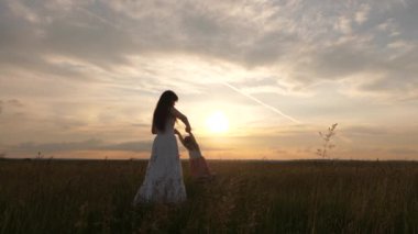 Mutlu çocuk gün batımında annesiyle uçuyor. Anne, sevgili çocuğunun ellerinde uçarken sağlıklı bir bebek gülüyor. Anne ve bebek yaz parkında. Özgür aile ve çocukluk kavramı