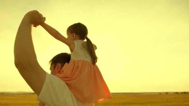 Vader draagt schouders van zijn geliefde kind, in zonnestralen. Vader loopt met zijn dochter op zijn schouders bij zonsondergang. kind met ouders loopt bij zonsondergang. gelukkig gezin rustend in het park. — Stockvideo