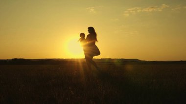 Çocuk gün batımında tarlada annesinin kollarında uçuyor. Anne kucağında küçük bir kızı, uçmakta olan sağlıklı bir çocuğu ile dönüyor. Aile ve bebek parkı. sağlıklı aile ve çocukluk kavramı