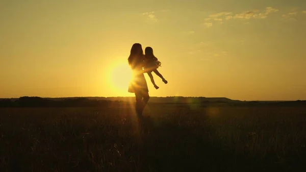 Kind spielt und fliegt im Arm der Mutter bei Sonnenuntergang auf dem Feld. Mutter wirbelt mit kleiner Tochter im Arm, gesundes Kind auf der Flucht. Familien- und Kleinkinderpark. Gesundes Familien- und Kindheitskonzept — Stockfoto