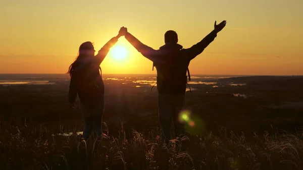 Voyageurs, un homme et une femme avec sac à dos, aller au bord de la colline dans les rayons de l'aube, lever la main, applaudir leurs mains et profiter de la victoire et beau soleil et paysage. concept de voyage familial et de tourisme — Photo