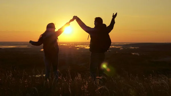 Voyageurs, un homme et une femme avec sac à dos, aller au bord de la colline dans les rayons de l'aube, lever la main, applaudir leurs mains et profiter de la victoire et beau soleil et paysage. concept de voyage familial et de tourisme — Photo