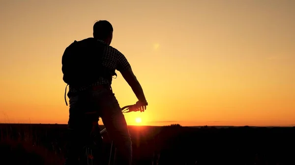 Un viaggiatore libero viaggia con una bicicletta al tramonto. concetto di avventura e di viaggio. ciclista solitario che riposa nel parco. Escursionista sano giovane va in bicicletta ai margini della collina, godendo della natura e del sole. — Foto Stock