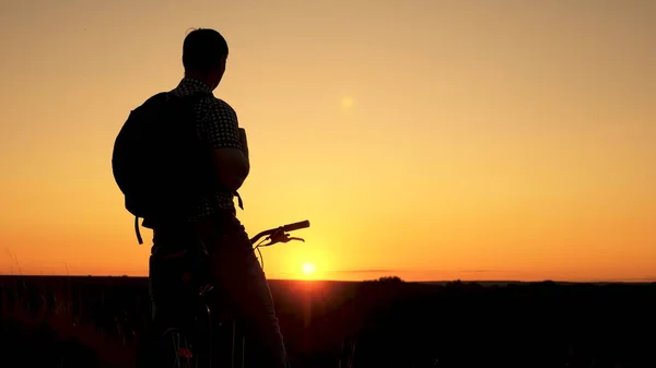 Un viaggiatore libero viaggia con una bicicletta al tramonto. concetto di avventura e di viaggio. ciclista solitario che riposa nel parco. Escursionista sano giovane va in bicicletta ai margini della collina, godendo della natura e del sole. — Foto Stock