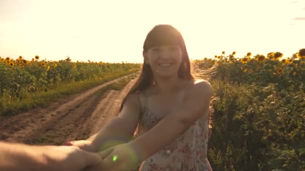 Dívka a kluk Rkuka v ruce, ve večerních hodinách procházka podél pole se slunečnicemi při západu slunce, držet se za ruce. Mladá dívka cestuje na venkově se svým přítelem, běhají přes pole kvetoucích slunečnic. — Stock video