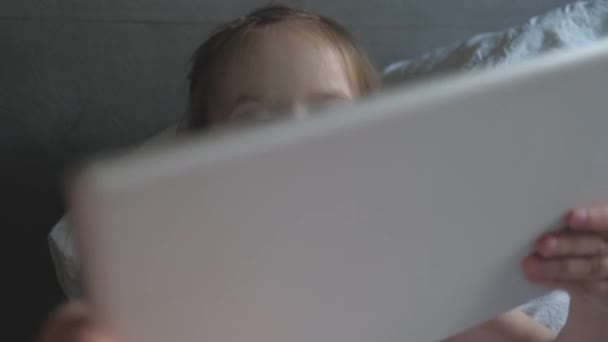 Piccola figlia gioca su uno smartphone. imparare in quarantena a casa utilizzando il tablet via Internet. Carino bambino guardando cartone animato utilizzando tablet. Covid auto-isolamento 19. bambina sul divano e gadget — Video Stock