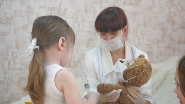 Barnet leker på sjukhuset. vilt låtsas vara läkare, sjuksköterska, veterinär, läker en patient med ett vaccin. Söt flicka ger en injektion till leksaksbjörnen. baby spelar i en medicinsk mask. — Stockvideo