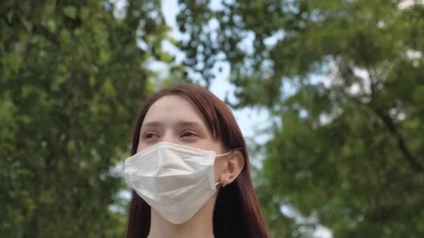 Şehirdeki kız tıbbi maskeyle seyahat ediyor. Park 'ta açık havada genç bir kızın yüzünde koruyucu maske var. Kadın turist yüzünü virüslerden koruyor. Yüzünde maskeyle caddenin aşağısından depoya git. — Stok video