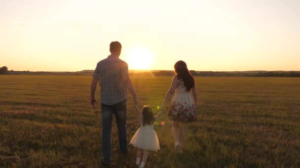 Dcera si hraje a skočí do pole, drží se za ruce mámy a táty. zdravá Happy rodina s dítětem procházky v parku při západu slunce. děti a rodiče chodí na sluníčko. koncept šťastné rodiny a dětství — Stock video
