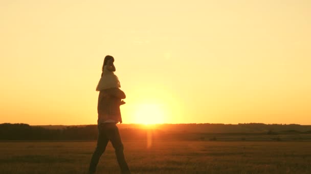 Vader draagt schouders van zijn geliefde kind, in zonnestralen. Vader loopt met zijn dochter op zijn schouders bij zonsondergang. kind met ouders loopt bij zonsondergang. gelukkig gezin rustend in het park. — Stockvideo