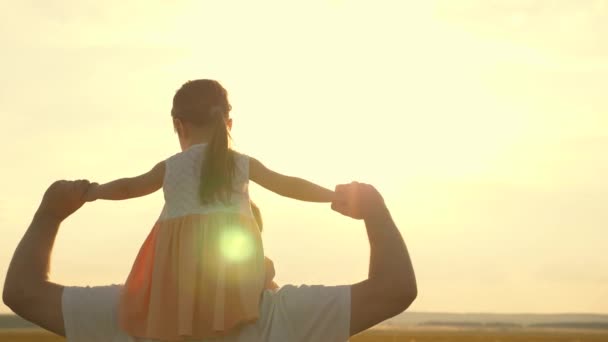 Szczęśliwa rodzina odpoczywająca w parku. Tata nosi ramiona swojego ukochanego dziecka, w promieniach słońca. Ojciec chodzi z córką na ramionach w promieniach zachodzącego słońca. dziecko z rodzicami spaceruje o zachodzie słońca. — Wideo stockowe
