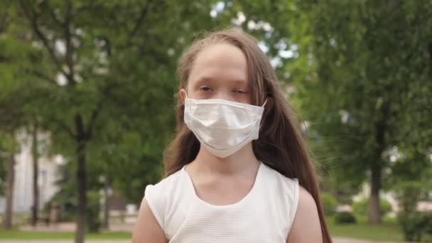 街中の女の子が医療マスクで旅をしてる。公園の屋外で若い女の子の顔に保護マスク。女の観光客は顔をウイルスから守る。顔を下の通りにマスクをして保管して — ストック動画