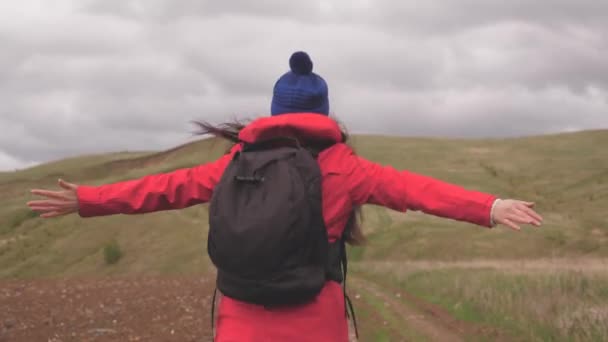 Die freie, glückliche Reisende geht mit offenen Armen in die Berge, Wind bläst ihr die Haare. junge gesunde Frau reist mit einem Rucksack und genießt die schöne Landschaft der Berge und Hügel. Reise und Abenteuer — Stockvideo