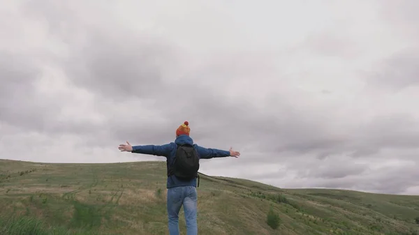 Livre viajante masculino feliz vai para montanhas com os braços abertos e redemoinhos. jovem cara saudável viaja com uma mochila desfrutando de belas paisagens de montanhas e colinas. conceito de viagem e aventura — Fotografia de Stock