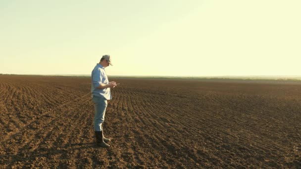 Granjero con tableta en el campo. agrónomo masculino comprueba la calidad del grano de siembra. El hombre de negocios revisa su campo. Un agricultor comprueba la calidad del suelo antes de sembrar . — Vídeo de stock