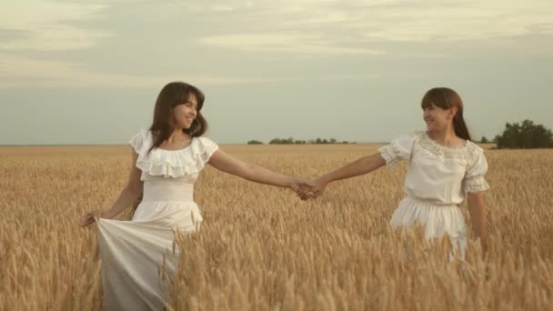 Figlia e madre si tengono per mano correndo lungo un campo di grano dorato. Al rallentatore. famiglia felice viaggia attraverso il campo, mano nella mano. concetto di famiglia felice e sana. bella madre e figlia adulta. — Video Stock