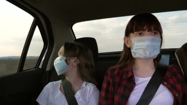 Здоровые девочки-подростки в защитной стерильной медицинской маске едут в такси. Понятие пандемического коронавируса. Бесплатные девушки путешествуют в масках в машине. защита от вирусов. дети ездят в машине — стоковое видео
