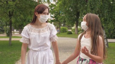 Dışarıda, parkta, koruyucu maskeli iki kız. Şehir sokaklarında tıbbi maske takan kızlar. Turist virüsü koruması. Dışarı çıkıp bakterilere karşı maskeli ol.