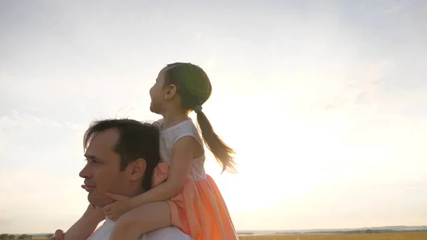 Criança com pais anda ao pôr-do-sol. Papai carrega nos ombros de seu filho amado, em raios de sol. O pai caminha com a filha sobre os ombros em raios de sol. família feliz descansando no parque . — Fotografia de Stock