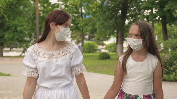 Twee meisjes met beschermende maskers op hun gezicht in een park. Meisjes op straat reizen in een medisch masker. bescherming van het toeristenvirus. gaan gemaskerd buiten tegen bacteriën — Stockfoto