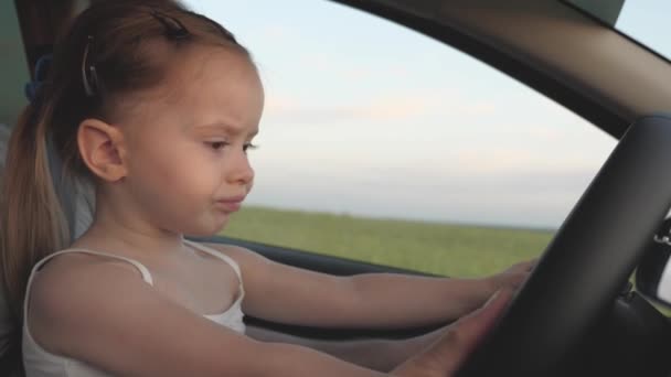 Papá le enseña a su pequeña hija a girar el volante mientras está sentado en su coche en el asiento del conductor. padre viaja con niños en coche. El conductor y el niño conducen. familia feliz y concepto de infancia — Vídeos de Stock