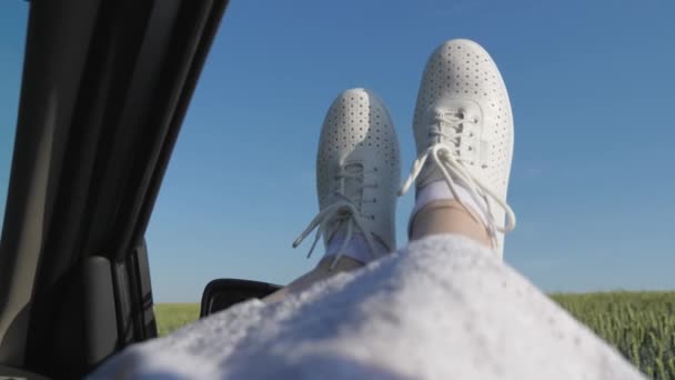 Free woman travels by car. healthy Young woman enjoys traveling by car, protruding her legs from an open window. Legs of a girl in car window, riding car on country road past wheat field.travel — Stock Video