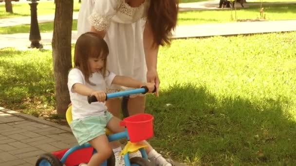 Genitori e figlioletta camminano nel parco. Mamma felice insegna alla figlioletta ad andare in bicicletta. Mamma gioca con il suo bambino all'aperto. concetto di una famiglia felice e l'infanzia. bambino impara ad andare in bicicletta . — Video Stock