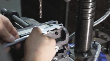 Tamirci atölyedeki kalibreleri ölçüyor. Çilingir atölyesindeki bir fabrikada işçi. Matkap, çalışanlar için matkap, düz çelik plaka ve matkap..