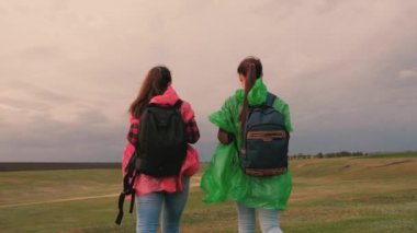 Sağlıklı kadın turistler renkli yağmurluklarla sırt çantalarıyla seyahat ederler. Ağır çekim. Gezginlerin takım çalışması. Özgür kızlar tepenin kenarına gider, sevinir, ellerini çırpar ve mutlulukla zıplarlar..