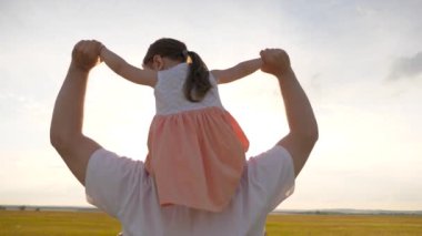 Baba gün batımında kızıyla birlikte omuzlarında yürüyor. Babam sevgili çocuğunun omuzlarını güneş ışınlarıyla taşır. Ailesi olan çocuk gün batımında yürür. Mutlu aile parkta dinleniyor..