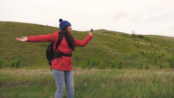 Здоровая веселая женщина путешествует и фотографирует природу по телефону. бесплатная девушка туристический блоггер записывает селфи видео у подножия гор с помощью смартфона с красивым пейзажем в фоновом режиме. — стоковое видео