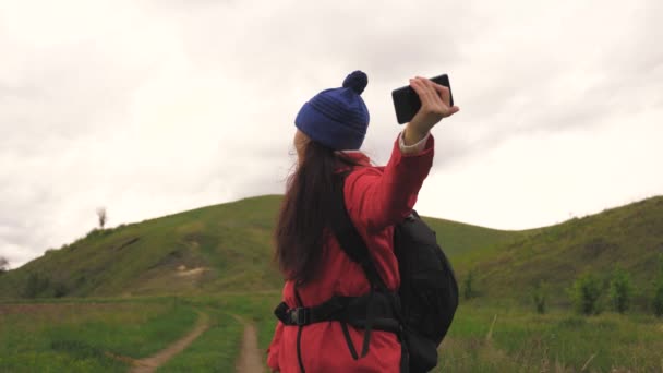 無料の若い女の子の観光ブロガーは、バックグラウンドで美しい風景とスマートフォンを使用して山のふもとに自撮りビデオを記録します.健康的な陽気な女性は電話で旅や写真の性質 — ストック動画