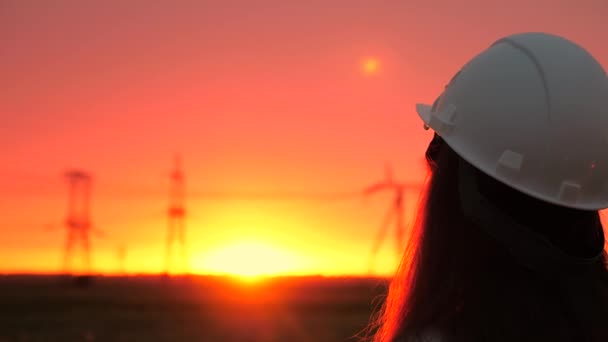 Beyaz kasklı bir kadın güç mühendisi bir elektrik hattını kontrol ediyor. Gün batımında yüksek voltajlı elektrik hatları. Dağıtım ve elektrik tedariği. temiz enerji — Stok video
